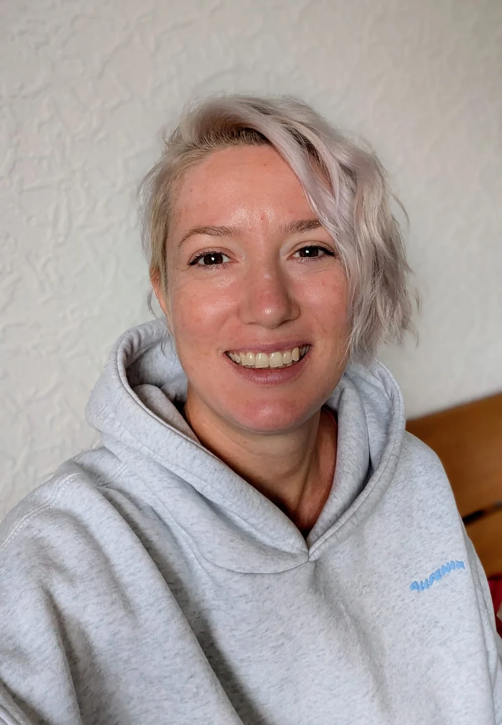 Samira Zepf mit kurzen hellen Haaren und grauem Kapuzenpullover, lächelnd